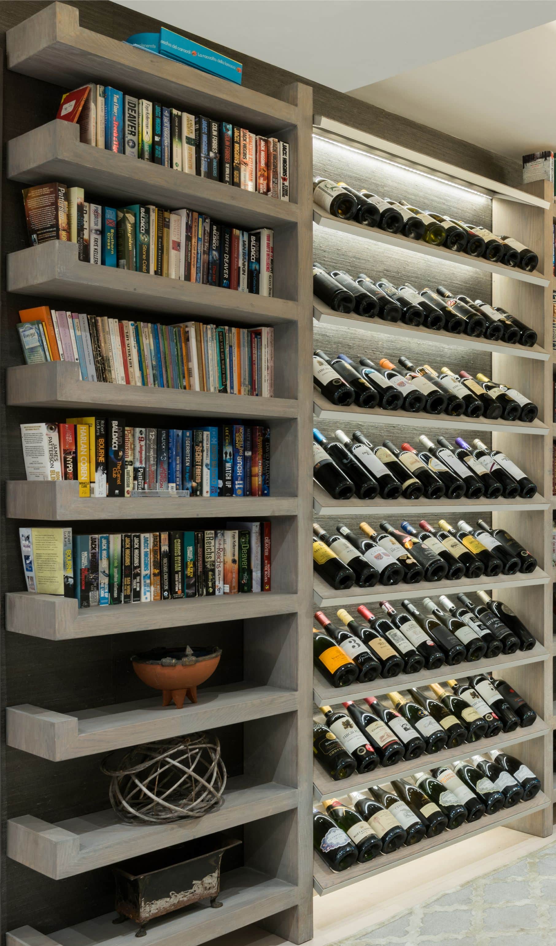 Weathered oak bookshelf beside a lit floor-to-ceiling wine wall