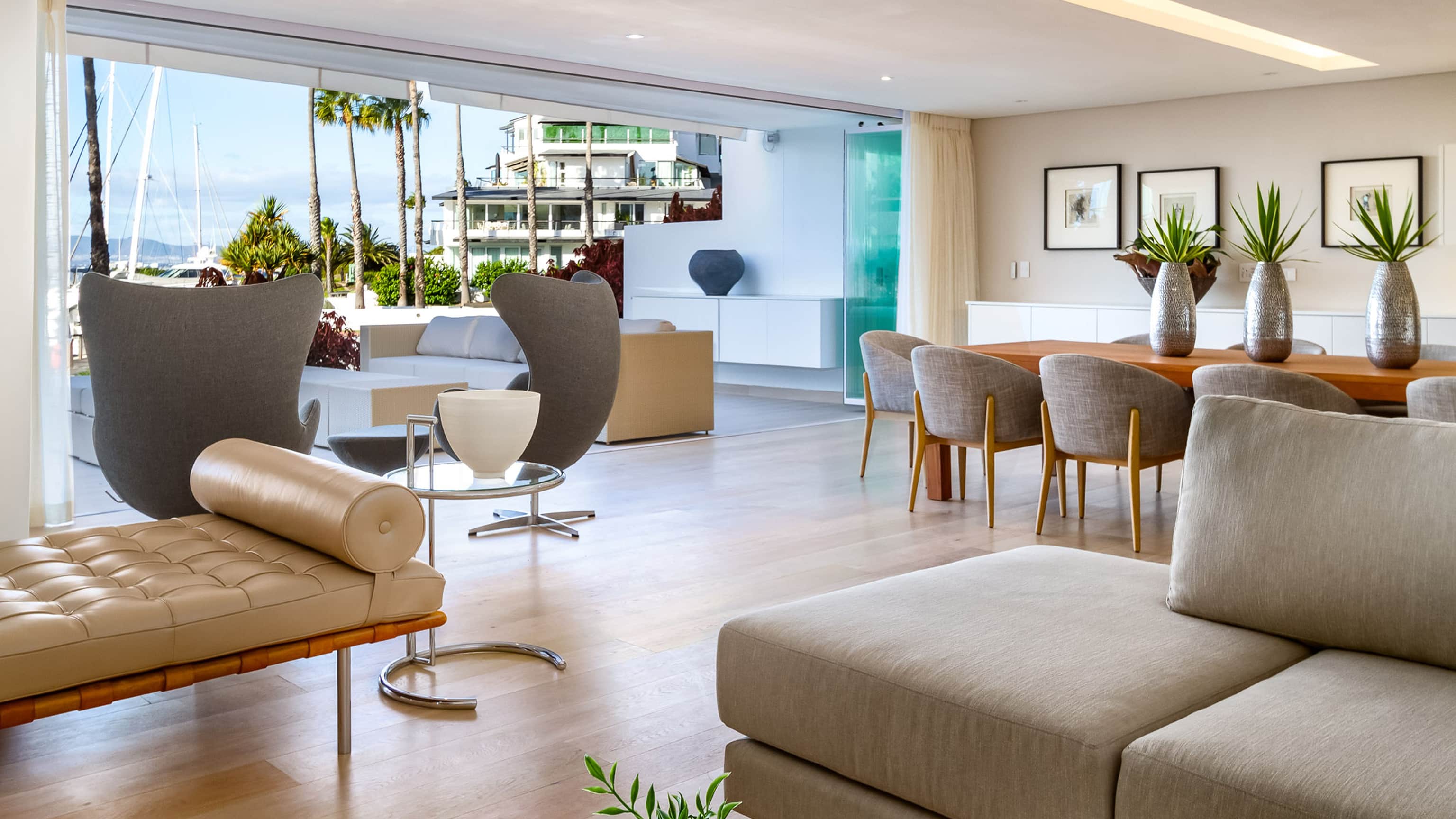 Living area with grey egg chairs and a tufted daybed, sliding windows open to the marina