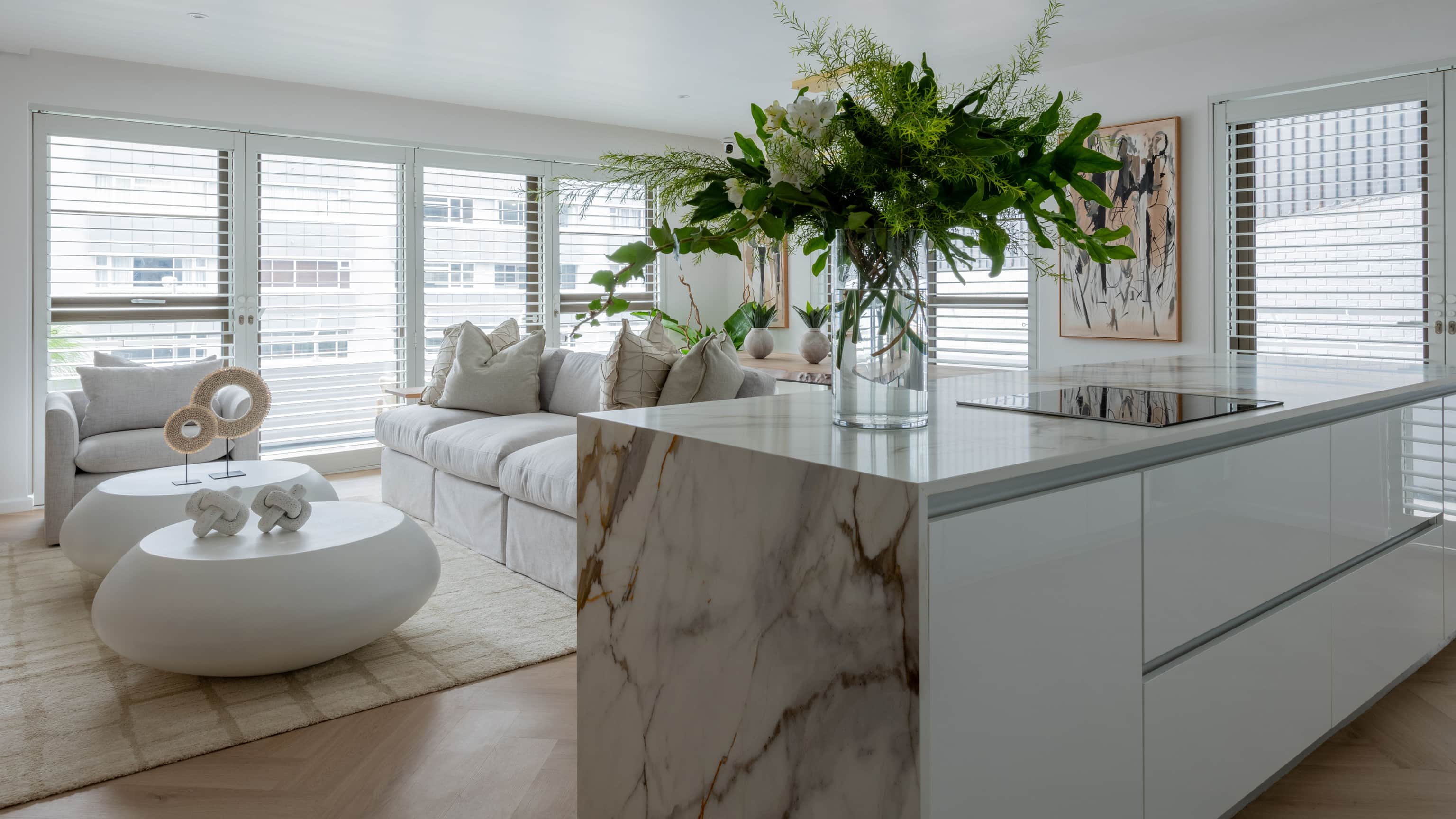 Open-plan living area with a marble kitchen island, white oval coffee tables and shuttered windows