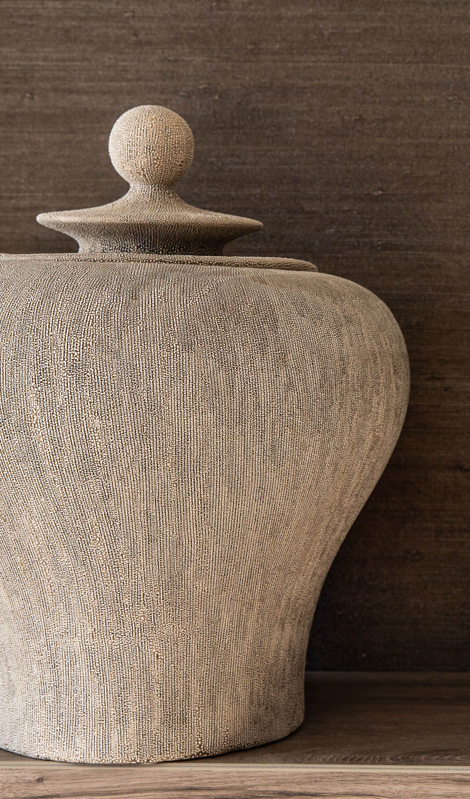 Textured stone urn with a lid against a grasscloth wall